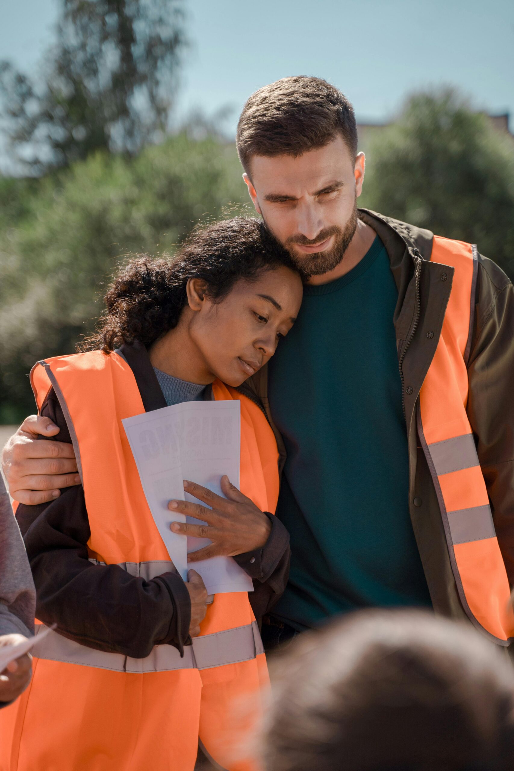 Pourquoi Nous Two people in safety vests embracing, reflecting teamwork and care.